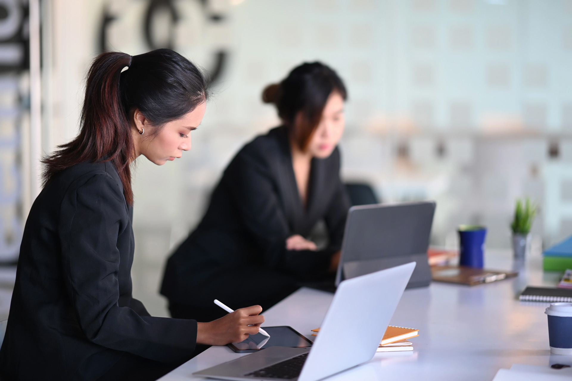 Duas mulheres trabalhando com notebooks e fazendo anotações em um tablet